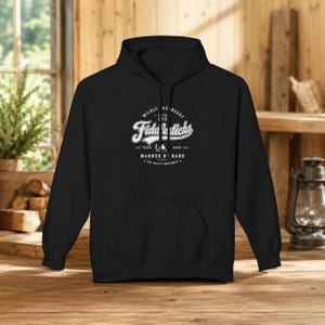 May include: A black hooded sweatshirt featuring a white graphic on the chest. The text reads MILDLY LEGENDARY ESTD 1913 Fiddlesticks TRADE MARK MARKED BY HAND THE PACIFIC NORTHWEST with a small clover icon centered within the circular design.