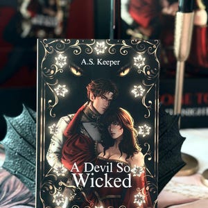 以下が含まれることがあります： A.S. Keeper著のペーパーバック「A Devil So Wicked」。正装した男女のイラストが描かれています。黒い背景に金のフィリグリー、白い花のアクセント、上部には光る黄色い目がデザインされた表紙です。