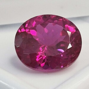 Può includere: Una gemma vibrante dal taglio ovale con una tonalità rosa magenta intenso e una superficie sfaccettata che riflette la luce. La pietra mostra un'elevata chiarezza e una lucentezza brillante, con tagli geometrici precisi su tutta la superficie.