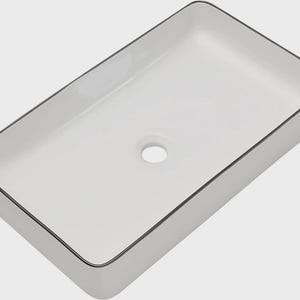 May include: A rectangular bathroom sink with a smooth white basin and a thin, dark gray rim around the top edge. The sink features a centered circular drain hole and has a clean, simple design with rounded corners and straight vertical sides.