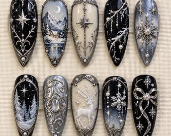 May include: A set of ten almond-shaped press-on nails featuring intricate winter-themed designs in black, white, silver, and cream. The nails are decorated with raised silver filigree, pearls, snowflakes, a deer, a cabin landscape, and stars.