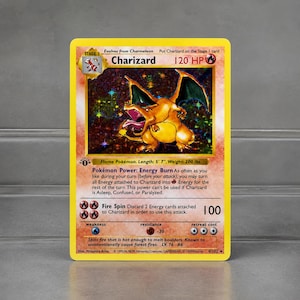 Peut inclure: Une carte à collectionner Pokémon Charizard. La carte présente une illustration vibrante de Charizard, une créature ressemblant à un dragon orange flamboyant, avec un fond holographique. Le texte de la carte comprend le nom "Charizard", les PV et les détails d'attaque. La carte mesure 170 cm de long et pèse 91 kg.