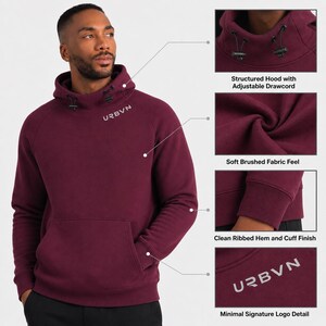 May include: A burgundy hoodie with a structured hood and adjustable drawcord. The hoodie features a soft, brushed fabric, a clean ribbed hem and cuff finish, and the URBVN logo detail. The model is wearing black pants.