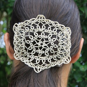Puede incluir: Un peine para el cabello de crochet blanco con un delicado diseño floral. El peine se lleva en el cabello castaño de una mujer.