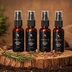 May include: Four amber glass spray bottles labeled Enigmatic, I Am, Intrinsic, and Pure. Each bottle contains 1 fl oz (30 ml) of natural fragrance spray and features a black pump cap. The bottles are arranged on a circular wooden slice.