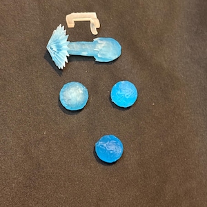 May include: A collection of small plastic accessories including a translucent white L-shaped bracket, a light blue projectile effect with a starburst tip, and three circular light blue textured discs of varying shades of blue.