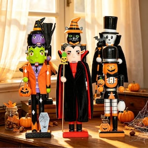 May include: Three wooden nutcrackers dressed for Halloween. The left figure is a green monster with an orange jacket and pumpkin bucket. The center figure is a vampire with a black cape and skull staff. The right figure is a pumpkin-headed character.