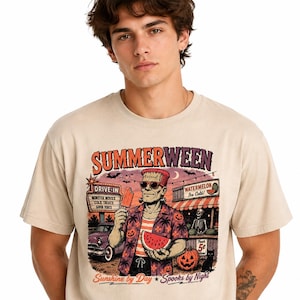May include: Beige t-shirt featuring a graphic with the text "SUMMERWEEN" and a Frankenstein-themed character holding watermelon and an ice pop. The graphic includes a drive-in movie scene and the text "Sunshine by Day * Spooks by Night."