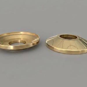 May include: Two circular brass escutcheon plates with a polished finish. One plate is shown from the underside, revealing a hollow interior and a central circular opening, while the other is shown from the top, featuring a smooth, sloped surface.