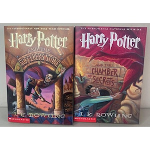 May include: Two hardcover books by J.K. Rowling titled Harry Potter and the Sorcerer's Stone and Harry Potter and the Chamber of Secrets. The covers feature colorful illustrations of a character with glasses, a red cape, and a large red bird.