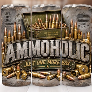 Peut inclure: Un gobelet cylindrique avec une impression graphique de munitions en laiton, une boîte à munitions en métal vert et le texte "AMMOHOLIC JUST ONE MORE BOX". Le design inclut "LIVE. LOVE. LOAD." et "SINCE 1776" avec un drapeau américain.