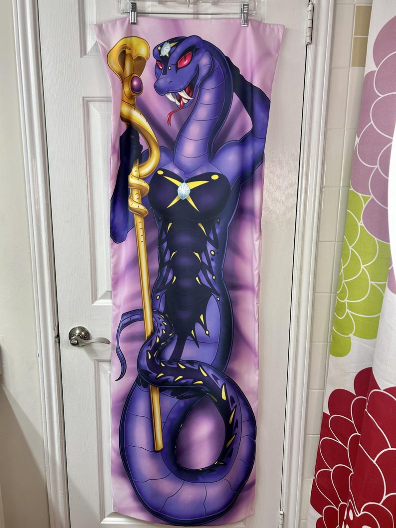 May include: A purple snake-like character with red eyes and a golden staff is depicted on a long, rectangular fabric. The character is wearing a dark outfit with a jewel. The background is a gradient of pink and purple.
