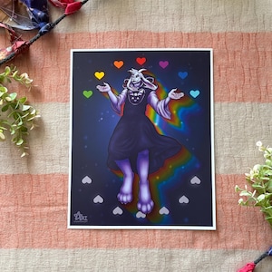 May include: A rectangular art print featuring a white, anthropomorphic goat character with long ears wearing a dark robe with a chest emblem. The character is surrounded by floating colorful hearts and a rainbow light effect against a dark background.