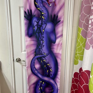 May include: A purple body pillow cover featuring a stylized snake illustration. The snake has yellow accents, red eyes, and an open mouth with a red tongue. The background is a tie-dye pattern of pink and purple.