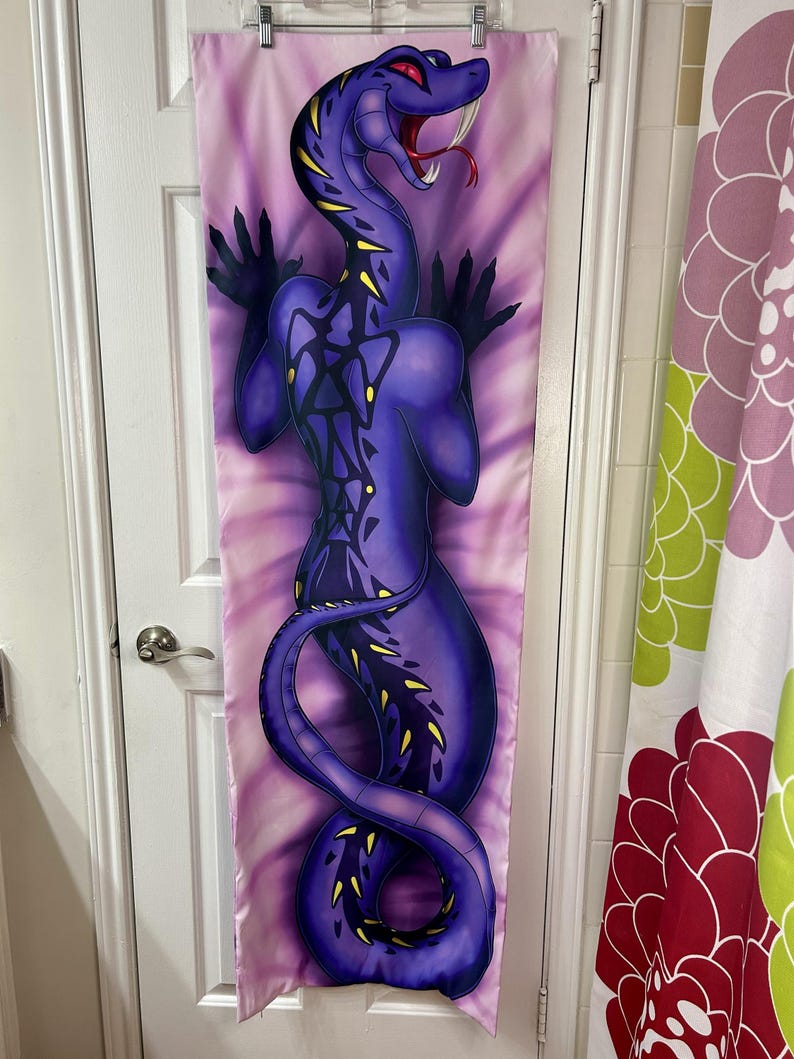 May include: A purple body pillow cover featuring a stylized snake illustration. The snake has yellow accents, red eyes, and an open mouth with a red tongue. The background is a tie-dye pattern of pink and purple.