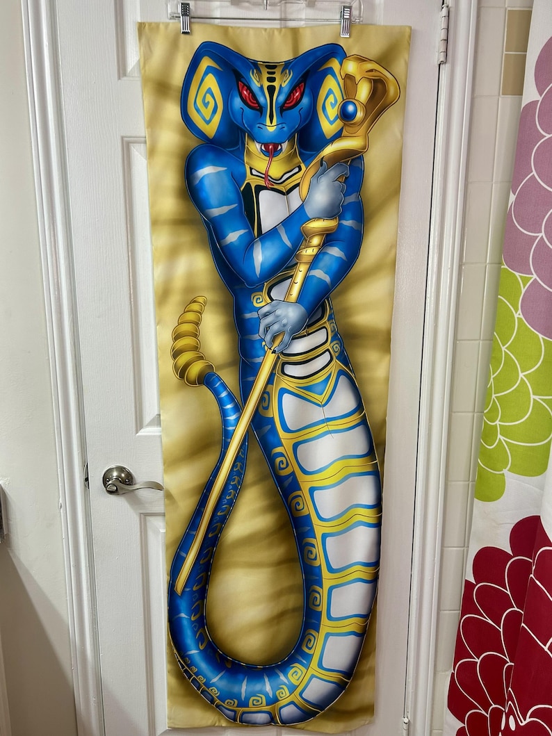 May include: A blue and gold decorative tapestry featuring a cobra-like figure holding a golden staff. The figure has red eyes and is set against a tan background. The tapestry is hanging on a door.