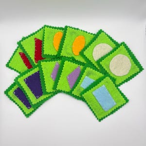 May include: A collection of green felt squares with zig-zag edges, each featuring a different shape in various colors. Shapes include red, orange, purple, blue, and white. The squares are arranged in a fan shape.