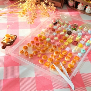 May include: A clear plastic storage container filled with a large assortment of miniature bread and pastry figurines in various shapes and colors, accompanied by a pair of white plastic tweezers for handling the tiny items.