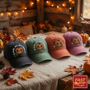 May include: Four baseball caps in charcoal, sage green, burnt orange, and mauve. Each cap features a graphic of a smiling jack-o'-lantern with a small black cat on top, surrounded by the text "OH, WELL... YOU'LL JOIN US SOMEDAY."