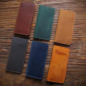 May include: Six rectangular leather wallets arranged in a group. The wallets are available in various colors including dark brown, forest green, tan, charcoal gray, navy blue, and light orange, each featuring a smooth finish and stitched edges.