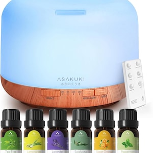 May include: A dome-shaped essential oil diffuser with a light blue glowing top and a wood-grain base featuring the brand name ASAKUKI. It includes a white remote control and six small brown glass bottles labeled Tea Tree, Lemongrass, Lavender, Eucalyptus, Sweet Orange, and Peppermint.