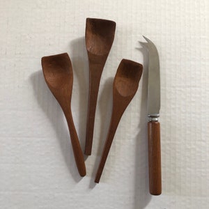 Pode incluir: Quatro colheres de madeira e uma faca de queijo. As colheres são de tamanhos e formas diferentes. A faca tem um cabo de madeira e uma lâmina de aço inoxidável.