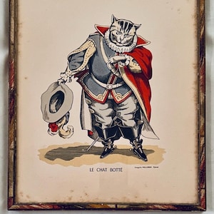 May include: Framed vintage print featuring a cat dressed in a historical costume, holding a hat. The cat wears a red cape, a white ruffled collar, and a gray and gold outfit. The print is in a decorative wooden frame.