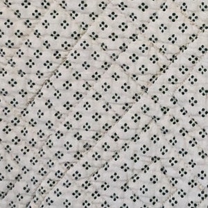 May include: Close-up of a white fabric with a repeating pattern of small, black floral-like shapes. The fabric is quilted with diagonal stitching, creating a diamond pattern across the surface.