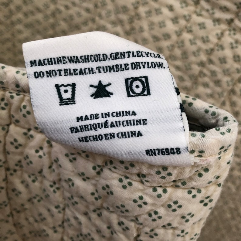 May include: A white fabric tag with care instructions and the text "MACHINE WASH COLD, GENTLE CYCLE. DO NOT BLEACH. TUMBLE DRY LOW." The tag also reads "MADE IN CHINA, FABRIQU&Eacute; AU CHINE, HECHO EN CHINA" and has the number RN76948.