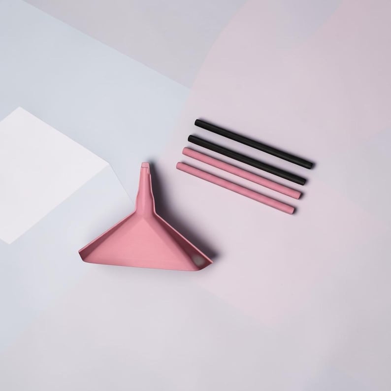 May include: A pink triangular funnel with a narrow spout positioned next to two black cylindrical straws and two pink cylindrical straws arranged in a parallel row. The items are displayed on a flat surface with geometric shapes in shades of pink and blue.