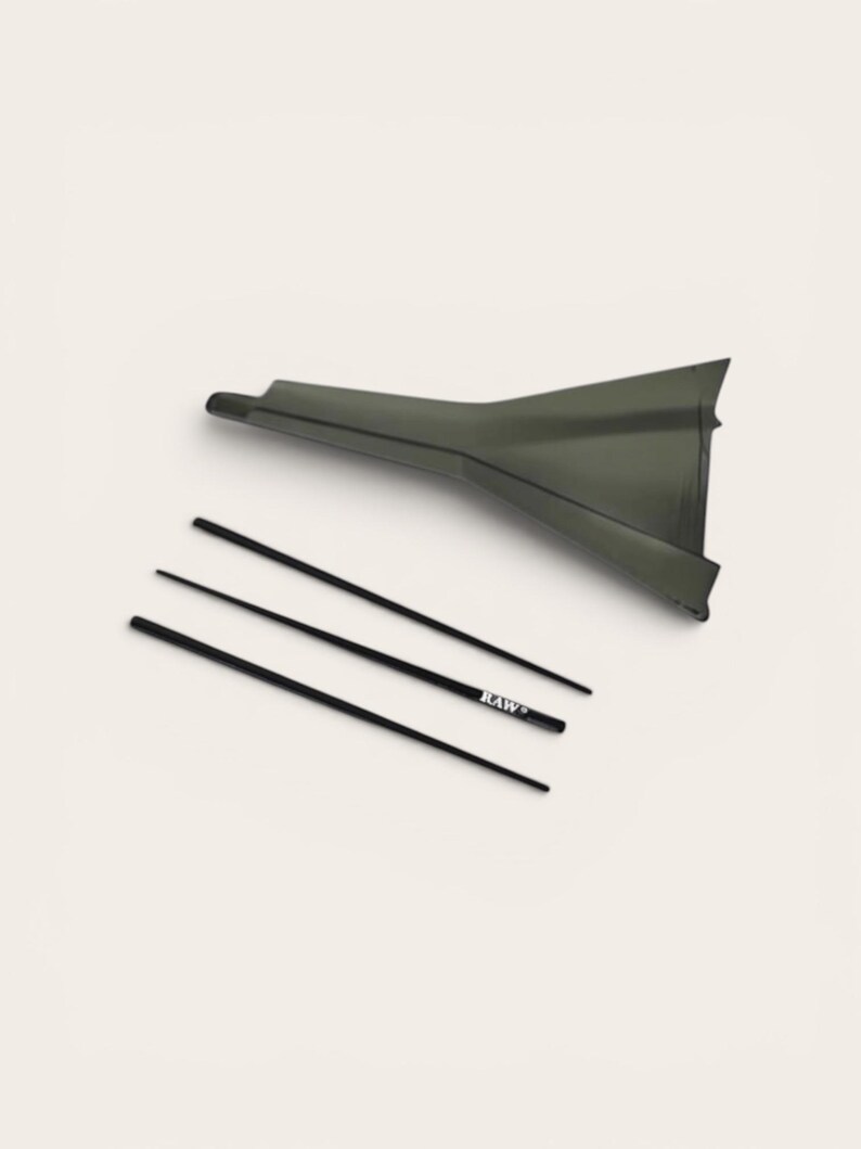 May include: A dark olive green plastic funnel with a wide opening and a narrow spout, accompanied by three thin black sticks. One of the sticks features the white text "RAW" printed clearly on its surface, indicating the brand name.