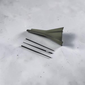 May include: A dark olive green plastic funnel with a wide, flared opening and a narrow spout, accompanied by three thin, black cylindrical rods. One of the rods features the white text "RAW" printed clearly on its surface.