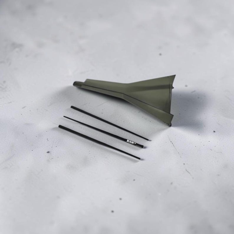 May include: A dark olive green plastic funnel with a wide, flared opening and a narrow spout, accompanied by three thin, black cylindrical rods. One of the rods features the white text "RAW" printed clearly on its surface.