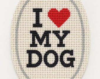 Może przedstawiać: Owalne płótno do haftu z czarnym wyszywanym napisem I, MY oraz DOG, z czerwonym wyszywanym symbolem serca zastępującym słowo LOVE. Wzór jest otoczony cienką szarą owalną ramką wyszytą na siatce w kolorze kremowym.