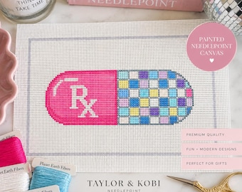 May include: A rectangular needlepoint canvas featuring a large pill graphic. The left side is solid pink with a white Rx symbol, while the right side displays a multi-colored grid pattern of blue, yellow, and purple squares. The canvas has a gray border.