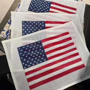 May include: Three rectangular needlepoint canvases featuring a printed American flag design. Each canvas displays a blue field with white stars and horizontal red and white stripes on a white mesh grid background, ready for embroidery stitching.