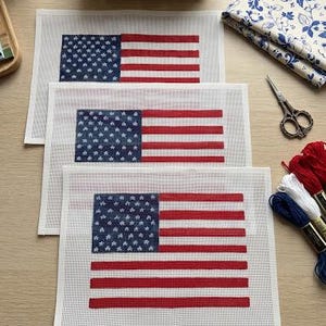 May include: Three rectangular needlepoint canvases featuring a printed American flag design with a blue field of white stars and horizontal red and white stripes. The canvases are white with a grid pattern and are arranged in a stacked formation.