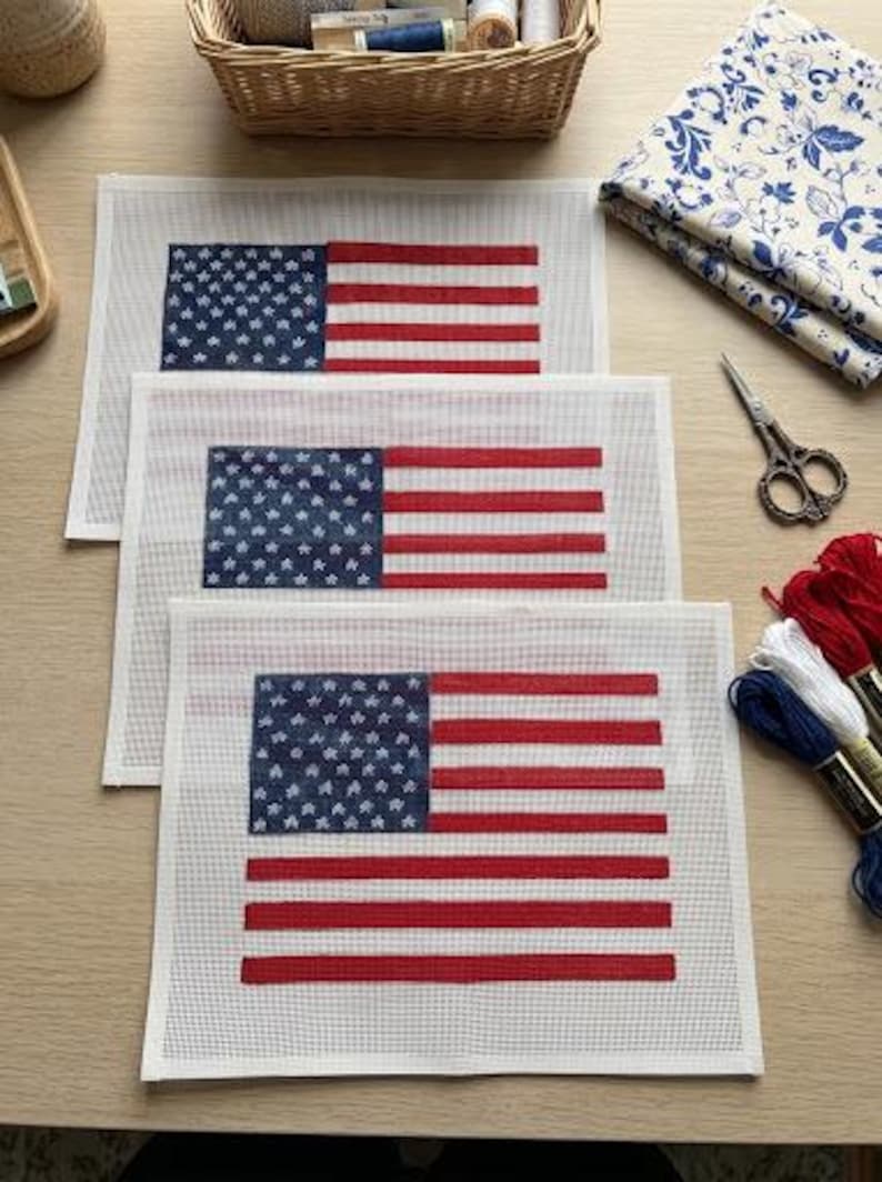 May include: Three rectangular needlepoint canvases featuring a printed American flag design with a blue field of white stars and horizontal red and white stripes. The canvases are white with a grid pattern and are arranged in a stacked formation.