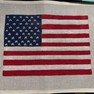 May include: A needlepoint canvas featuring a printed design of the United States flag. The design includes a blue canton with white star outlines and alternating horizontal red and white stripes, all set against a white grid mesh background.