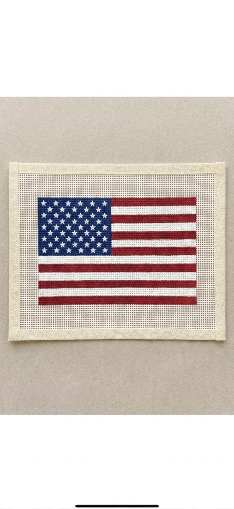 May include: A rectangular needlepoint canvas featuring the United States flag design. The flag consists of a blue canton with white stars and alternating red and white horizontal stripes, all set against a plain, unstitched cream-colored border.