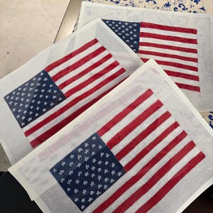 May include: Three rectangular needlepoint canvases featuring the American flag design. Each canvas displays a blue field with white stars in the upper left corner and alternating horizontal red and white stripes across the remaining surface area.