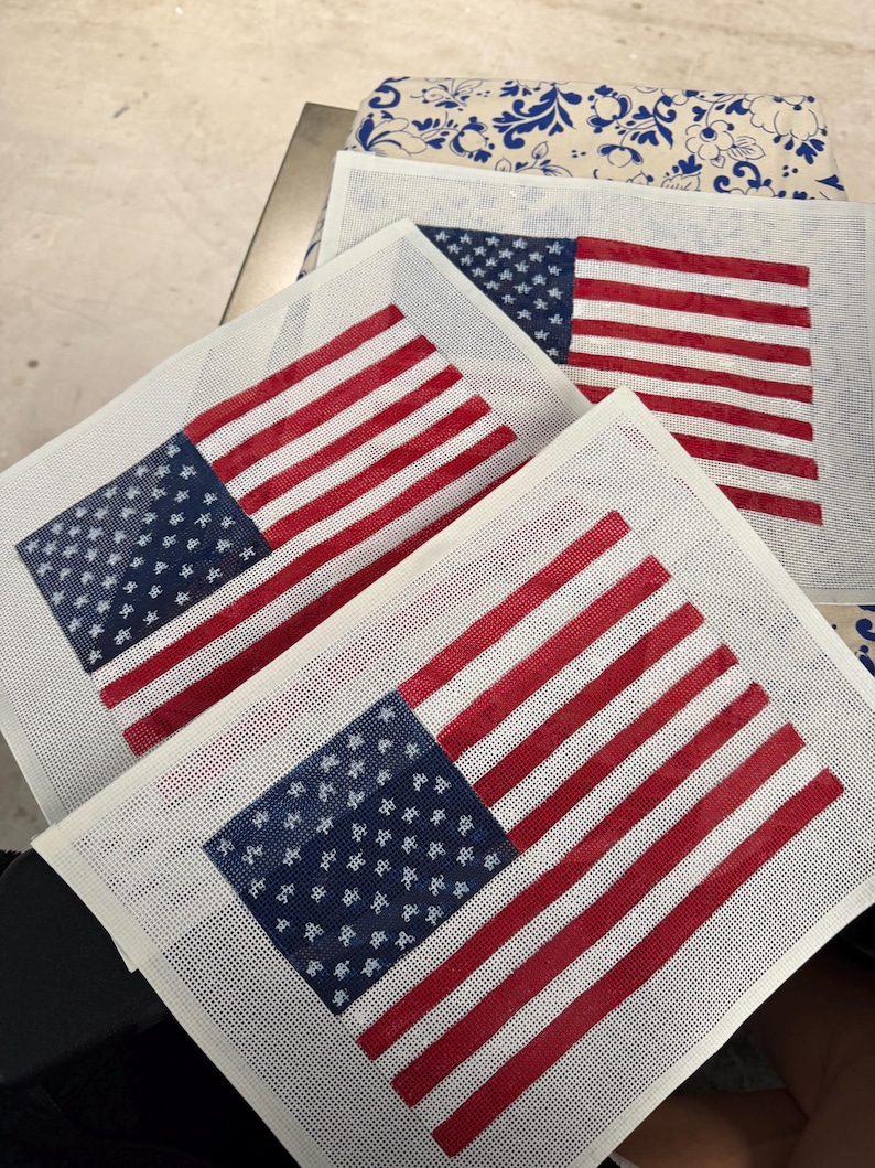 May include: Three rectangular needlepoint canvases featuring the American flag design. Each canvas displays a blue field with white stars in the upper left corner and alternating horizontal red and white stripes across the remaining surface area.