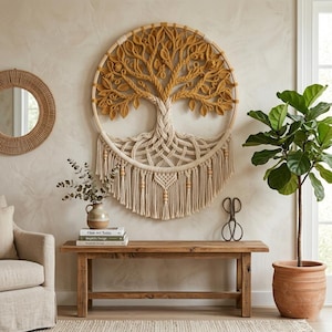 Op de afbeelding: Een ronde macramé wandhanger met een boomontwerp met mosterdgele bladeren en een crèmekleurige stam en wortelstelsel. Het kunstwerk is bevestigd aan een houten ring en is voorzien van lange, geknoopte franjes met houten kralen.