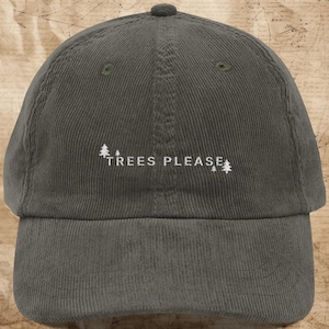 May include: A dark gray corduroy baseball cap featuring white embroidered text that reads TREES PLEASE, flanked by small white embroidered pine tree icons on both sides of the lettering. The cap has a structured crown and a curved brim.