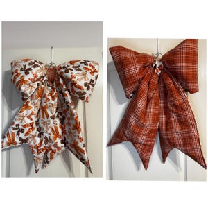 May include: Two large fabric bows hanging from hooks. The left bow features a white background with a repeating pattern of small brown and orange bows. The right bow is made of a solid orange and white plaid fabric with a distinct checkered pattern.