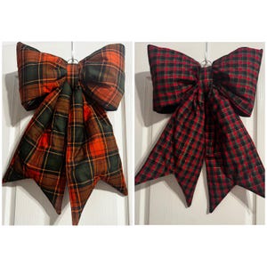 Puede incluir: Dos lazos decorativos de tela con patrones de cuadros. El lazo izquierdo muestra un tartán a gran escala en tonos naranja, verde oscuro y negro. El lazo derecho presenta un patrón de cuadros rojo, verde y negro con hilos dorados metálicos.