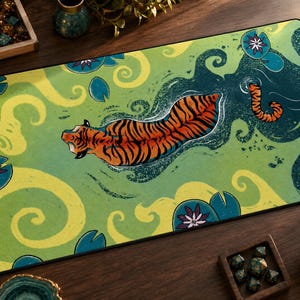 May include: A rectangular desk mat featuring a top-down illustration of an orange and black tiger swimming through green water. The scene includes swirling yellow currents, dark teal lily pads, and purple water lily flowers across the surface.