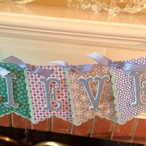 May include: A blue and white banner with the word "Believe" spelled out in blue letters. The banner is decorated with snowflakes and polka dots.