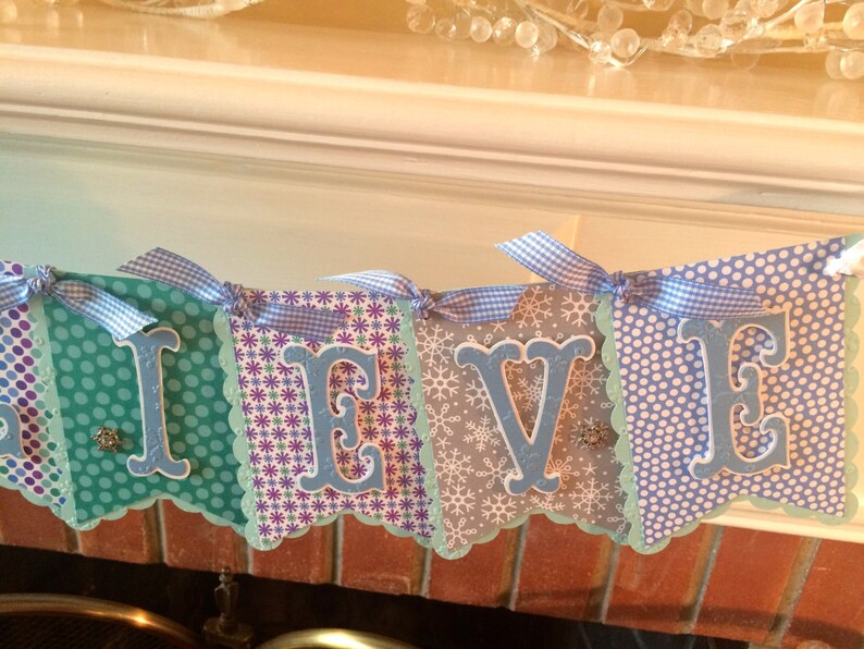 May include: A blue and white banner with the word "Believe" spelled out in blue letters. The banner is decorated with snowflakes and polka dots.