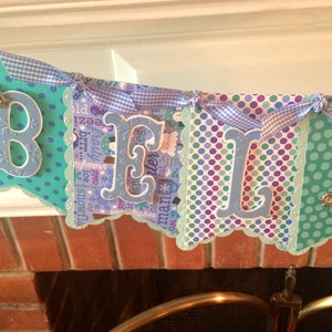May include: A blue and green banner with white polka dots and the word "Believe" spelled out in large, blue letters. The banner is decorated with white and blue gingham ribbon.